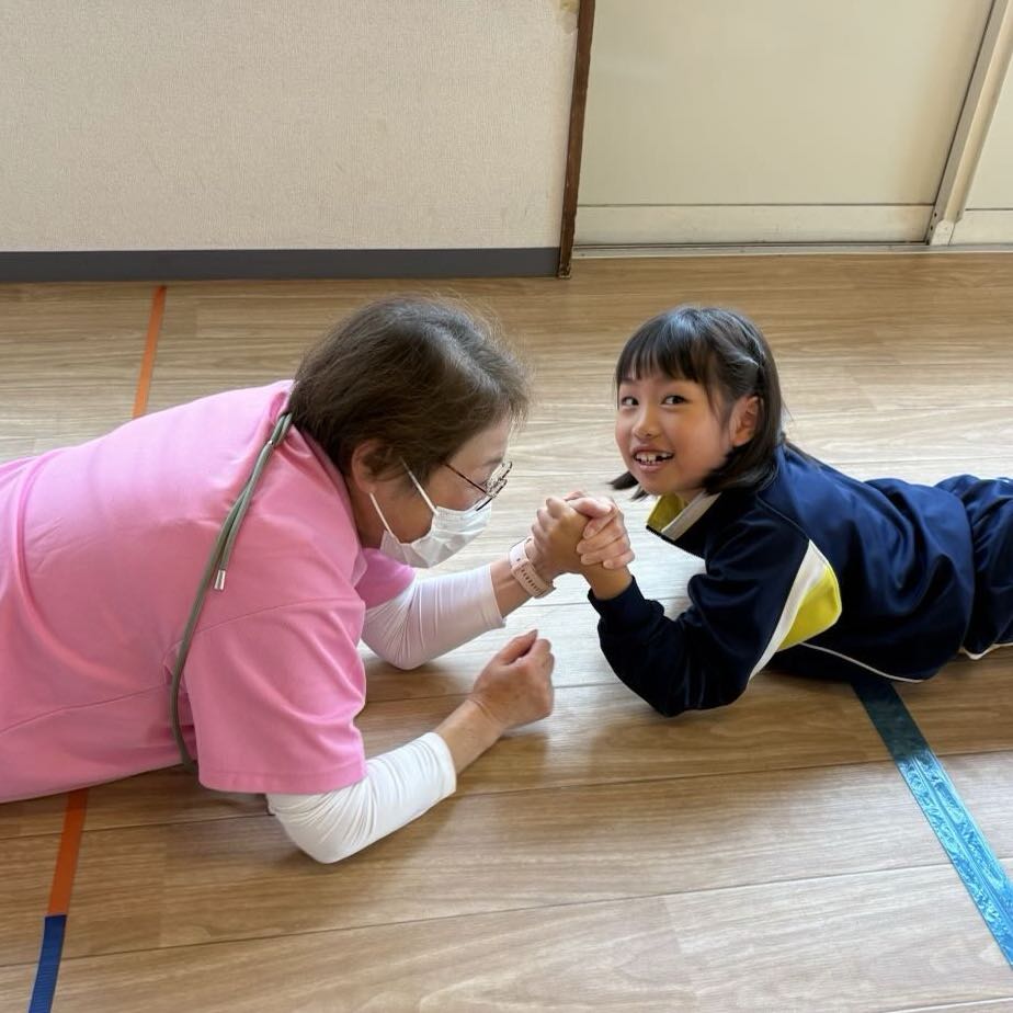 床に寝そべった子どもと目線を合わせ、手をつないで関わるスタッフ