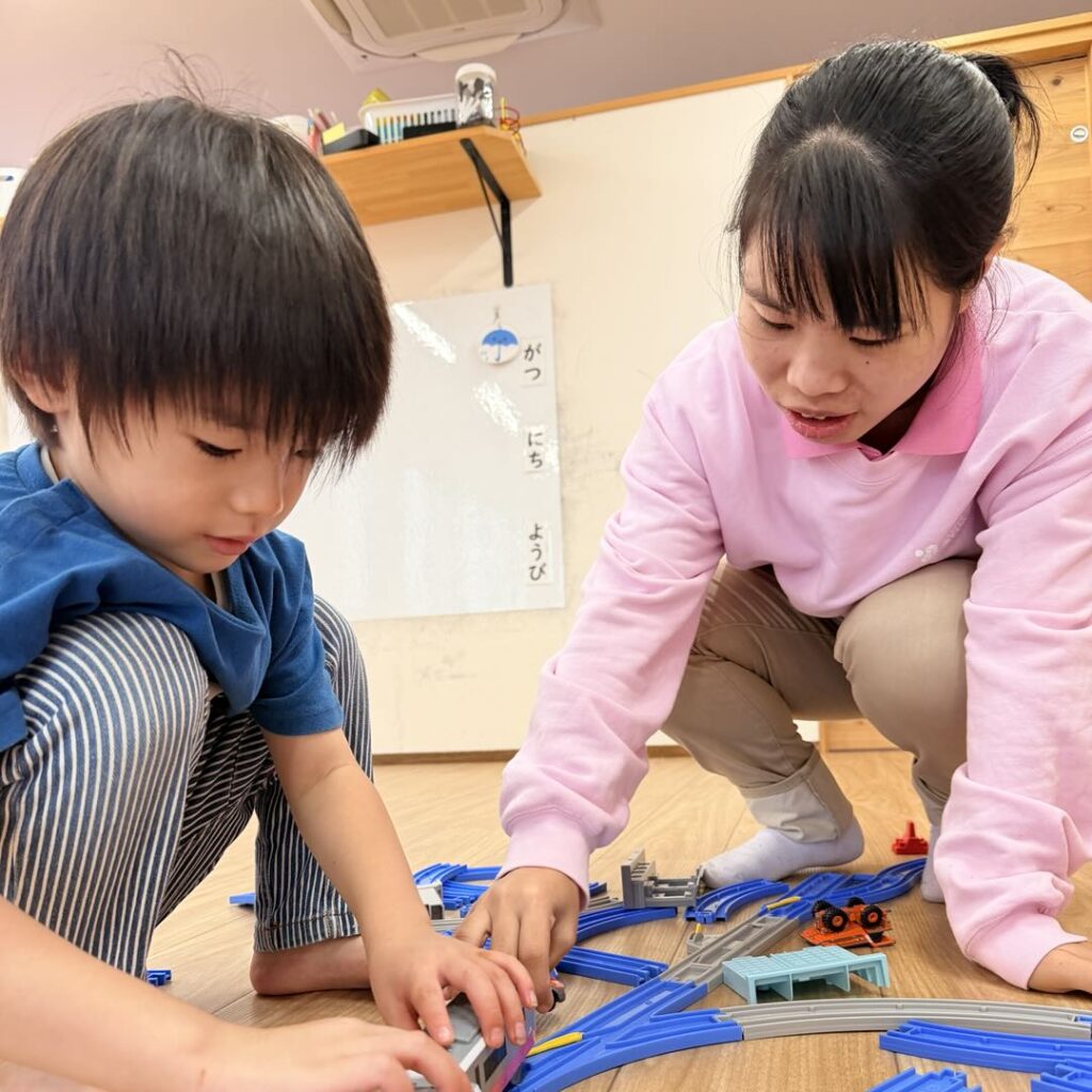 電車のおもちゃで遊ぶ子どもに寄り添うスタッフ