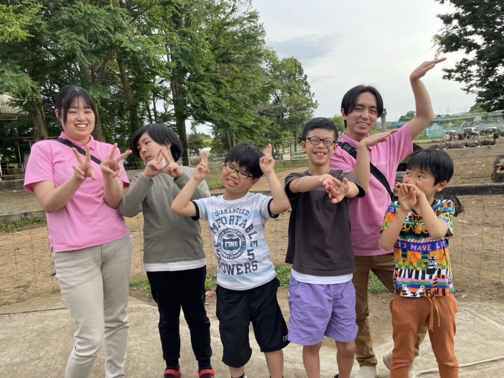 牧場へのお出かけで、ピースをするあていんぷらすわんのスタッフと子どもたち